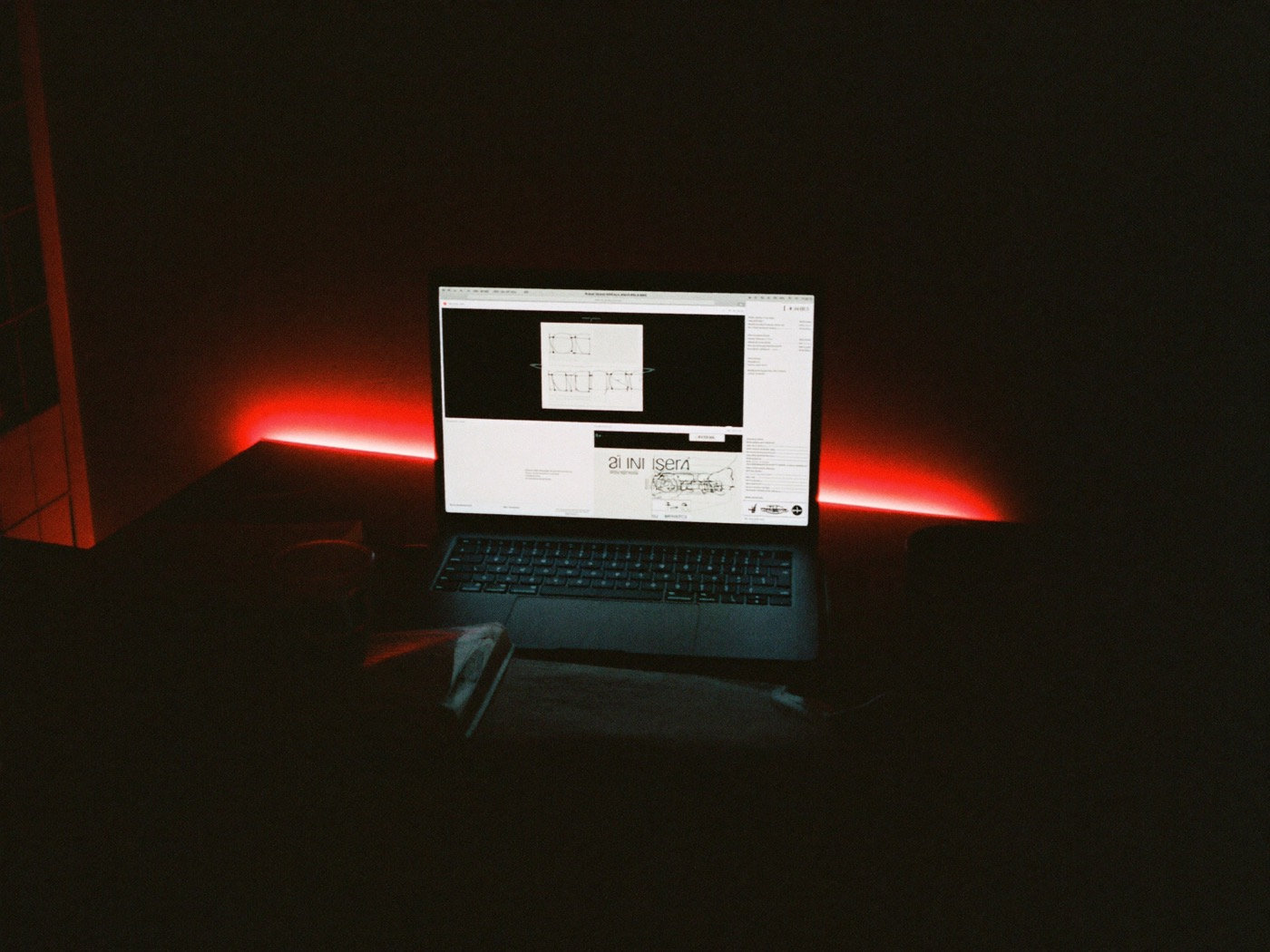 Mesa de trabalho à noite, iluminada pela tela do notebook e por uma luz vermelha ao fundo